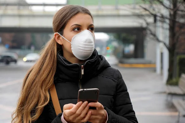 COVID-19 Pandemic Coronavirus Mobile Application - Young Woman Wearing Face Mask Using Smart Phone App in City Street to Aid Contact Tracing in Response to the 2019-20 Coronavirus Pandemic