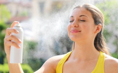 Young woman spraying Thermal Water on her face outside. Thermal water used for skin care, fix makeup, help skin irritation, redness and insect bites. clipart