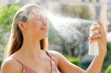 Genç bir kadın yüzüne termal su püskürtüyor. Cilt bakımı, makyaj, cilt tahrişi, kızarıklığı ve böcek ısırıkları için kullanılan termal su..