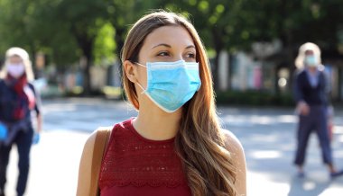 Şehir sokaklarında SARS-CoV-2 virüsüne karşı cerrahi maske takan COVID-19 Sosyal Mesafeli Kadın. Yüzü maskeli kız 2019 Salgın Koronavirüs Hastalığı sırasında sosyal mesafeye saygı göstererek yürüyor..
