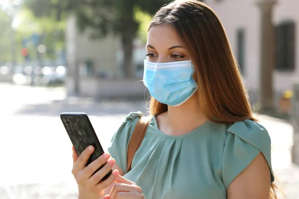 COVID-19 Pandemic Coronavirus Young Woman Wearing Surgical Mask Using Smart Phone App in City Street to Aid Contact Tracing in Response to the Pandemic Coronavirus