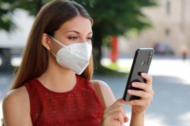 KN95 FFP2 maskeli COVID-19 Genç Kadın Coronavirus Hastalığı 2019 'a tepki olarak Kişinin İzlenmesine ve Kendine Teşhis Etmesine Yardım Etmek İçin Şehir Caddesinde Akıllı Telefon Uygulaması Kullanıyor