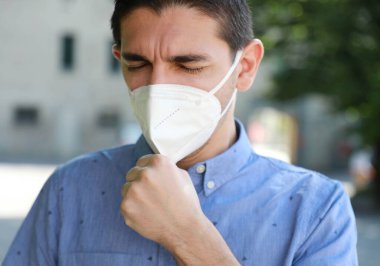 COVID-19 Salgın Coronavirüs Hastalıklı Adam KN95 FFP2 maskeli Şehir Caddesinde Öksürüyor. Dışarıda öksüren SARS-CoV-2 maskeli bir adamın portresi..