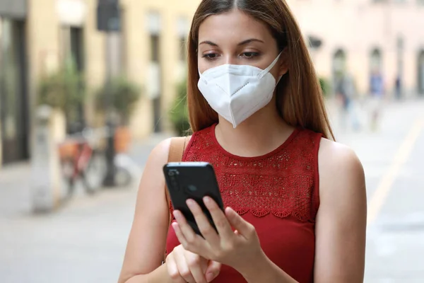 COVID-19 Portrait of Young Woman Wearing KN95 FFP2 Mask Using Smart Phone App in City Street to Aid Contact Tracing and Self Diagnostic in Response to Coronavirus Disease 2019