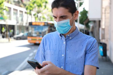 Cerrahi maskeli bir adam internet üzerinden akıllı telefonuyla şehir ulaşımı hakkında bilgi güncelliyor. Çevrimiçi bilet servisi, Salgın Koronavirüs sırasında cep telefonuyla ulaşım için ödeme yapıyor..