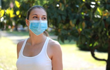 Parktaki COVID-19 Sportif kız SARS-CoV-2 virüsünü yaymak için tıbbi maske takıyor. Coronavirus Hastalığı 2019 'a karşı koruyucu maskeli bir kadın. Boşluğu kopyala.