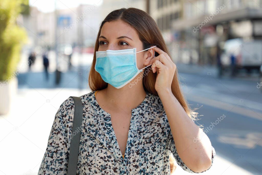 Girl in the street puts on a medical mask. Young business woman wearing surgical mask walking in city street.