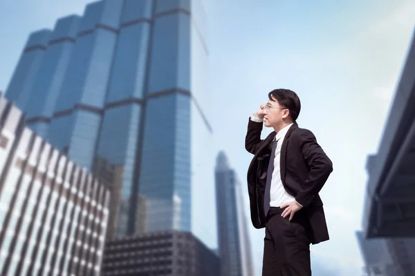 Уверенный азиатский бизнесмен стоит и смотрит на город — стоковое фото