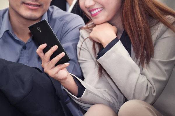 Asian business woman and man smiling and using cell phone togeth — Stock Photo, Image