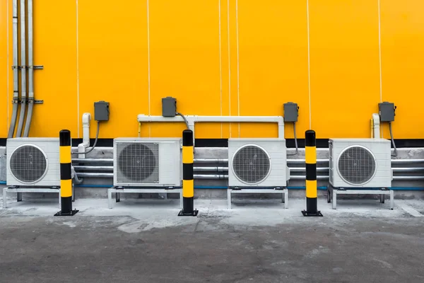 Compresor de aire acondicionado instalado fuera del edificio con poste de advertencia amarillo y negro en el suelo —  Fotos de Stock