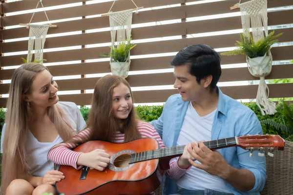 father teach daughter play guitar or music and mother sitting on