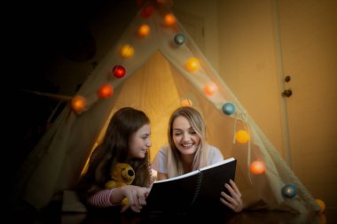 Mutlu küçük kız ve anne gülümsüyor ve birlikte kitap okuyorlar.