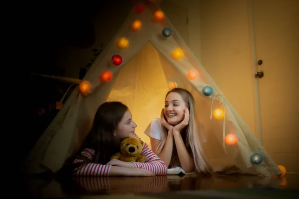Glad liten flicka och mor ler och spela camping i tält en — Stockfoto