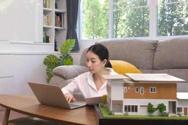 İş kadını mimarisi dizüstü bilgisayar ve tasarım üzerinde çalışıyor. Evdeki oturma odasında ev modeli ile birlikte çevik çalışıyor.