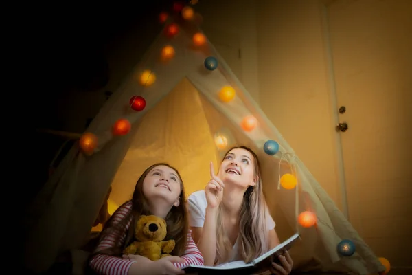 Glad liten flicka och mor ler och läser bok tillsammans och — Stockfoto