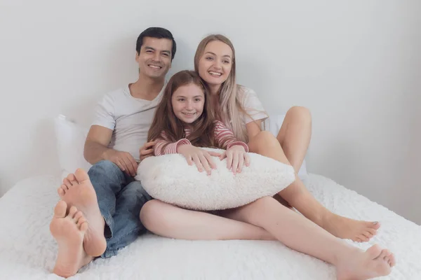 Niña sonriendo con madre y padre en la cama juntos en ser —  Fotos de Stock