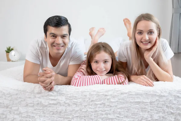 Niña sonriendo con madre y padre en la cama juntos en ser —  Fotos de Stock