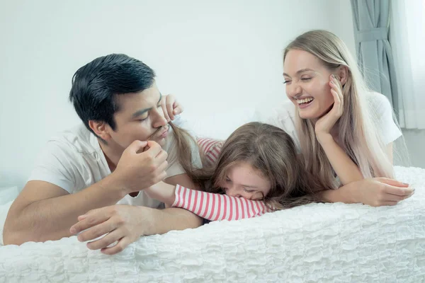 Liten flicka ler med mor och far på sängen tillsammans i vara — Stockfoto