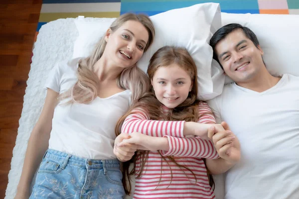 Niña sonriendo con madre y padre en la cama juntos en ser —  Fotos de Stock
