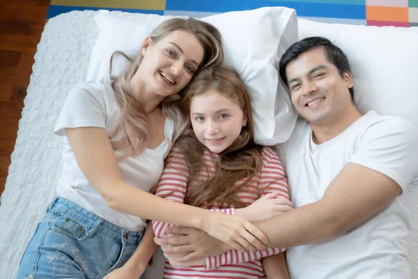 Niña sonriendo con madre y padre en la cama juntos en ser —  Fotos de Stock