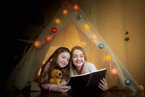 Gelukkig klein meisje en moeder glimlachen en samen lezen boek in t — Stockfoto