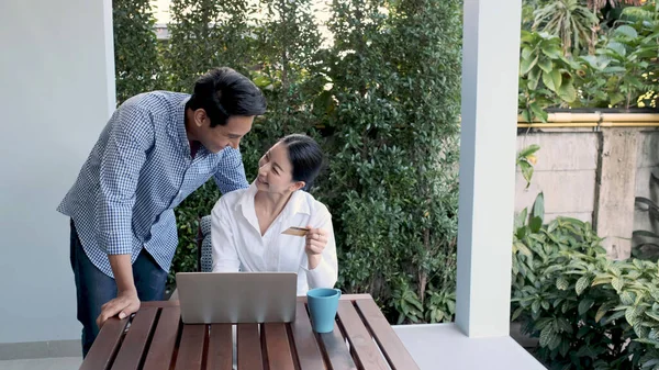 Mujer trabajadora y hombre casual que trabaja con el ordenador portátil y utilizar la tarjeta de crédito para el mercado de compras en línea en la terraza cerca del jardín en casa —  Fotos de Stock