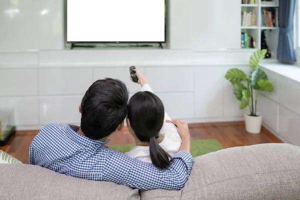 Back view of young family, man and woman watching TV together in