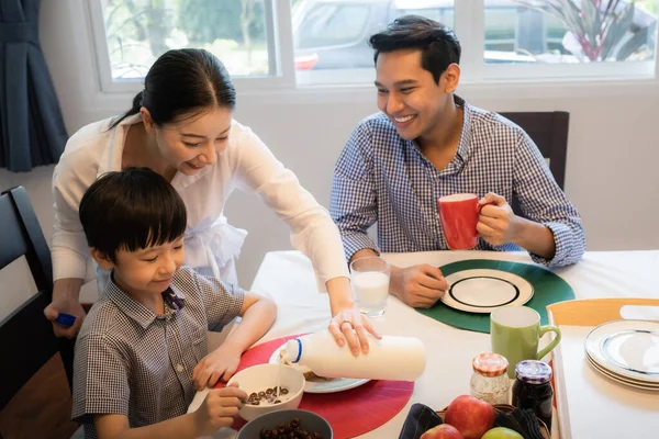 Asian family, mother pouring milk for son having breakfast toget