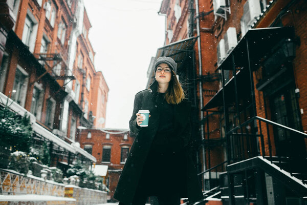 Вид спереди женщины, стоящей на зимней улице с чашкой кофе в руке и смотрящей в камеру
