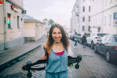Semt longboard elinde ile cadde üzerinde duran hipster gülümseyen kadın yarım uzunluk görünümünü