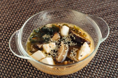 Kahverengi bir tabloda şeffaf bir kasede Japon çorbası