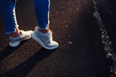 Ne tarafa gideceğimize karar verelim. Lastik yolda yürü. Kot pantolon ve gri spor ayakkabılı kadın bacakları. Ayakların gölgesi yerde..