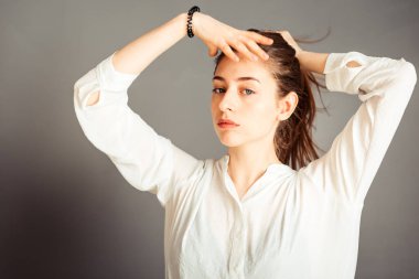 Odaklanmış kız saç stili yapıyor, gri arka planda at kuyruğu, yakın plan. Makyajsız, rötuşsuz.