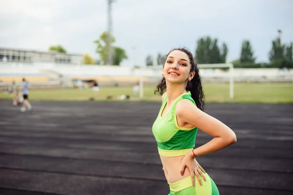 漂亮的卷曲女孩在体育场里伸展肌肉 这个女孩参加体育活动 浅绿色运动服 横向照片 — 图库照片