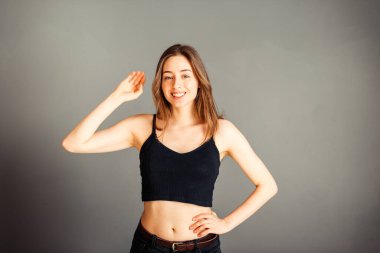 Siyah bluzlu, saçları sallanan ve gülümseyen gri arka planda bir kız. Makyajsız, rötuşsuz.