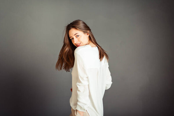 Young girl in a white shirt on a gray background. French woman in white blouse against a background of gray walls. Without retouching.