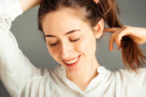 Usmívající Dívka Spokojeným Obličejem Drží Vlasy Rukama Šedém Pozadí Zblízka — Stock fotografie