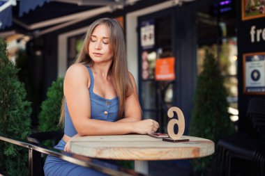 Güzel, uzun saçlı bir kız, bir kafede, ahşap yuvarlak bir masada oturuyor. Kafede birini bekle, bir emir bekle. Mavi bluzlu kız..