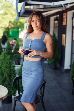 İnce bir kız elinde fincanla Avrupa 'da bir kafede duruyor. Spor kızı. Hayattaki spor eğitmeni