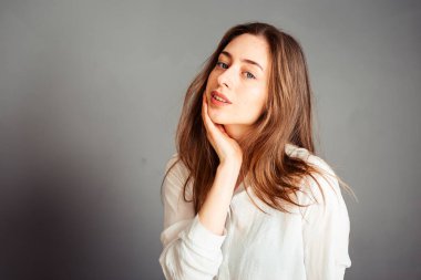 Gülümseyen kız, gri arka planda elleri yüzüne yakın, kapat. Makyajsız, rötuşsuz.