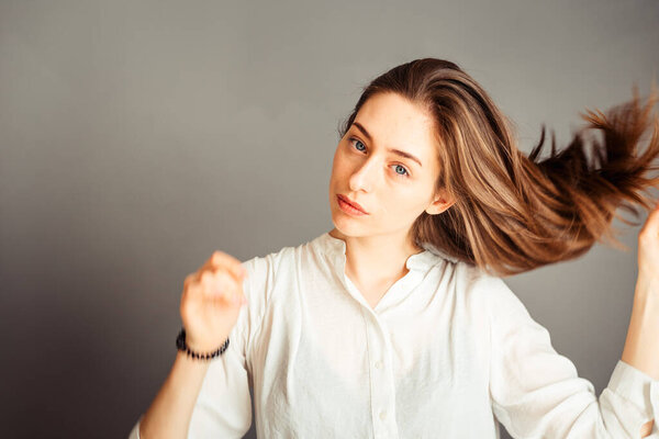 Сосредоточенная девушка делает прическу, хвостик на сером фоне, крупным планом. Без макияжа, без ретуши
.