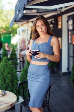 İnce bir kız elinde fincanla Avrupa 'da bir kafede duruyor. Spor kızı. Hayattaki spor eğitmeni