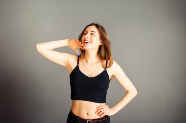 Siyah bluzlu, saçları sallanan ve gülümseyen gri arka planda bir kız. Makyajsız, rötuşsuz.