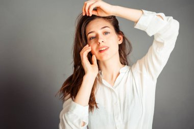 Gülümseyen kız, gri arka planda elleri yüzüne yakın, kapat. Makyajsız, rötuşsuz.