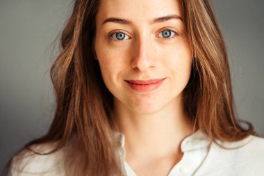 Gri arka planda beyaz gömlekli gülümseyen genç bir kızın yakın plan portresi. Ellerini yüzüne koy. rötuş ve makyaj olmadan.