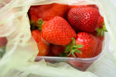 Plastik bir kutuda organik çilekler ve poşetler. Organik ürünlerin teslimatı. Doğal çilek ambalajı.