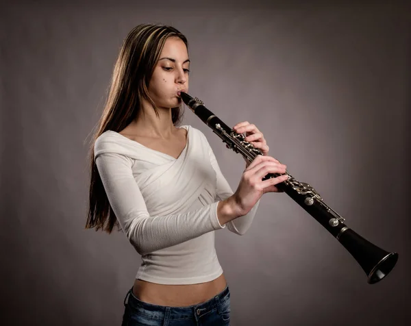 年轻女子在灰色背景下吹单簧管 — 图库照片