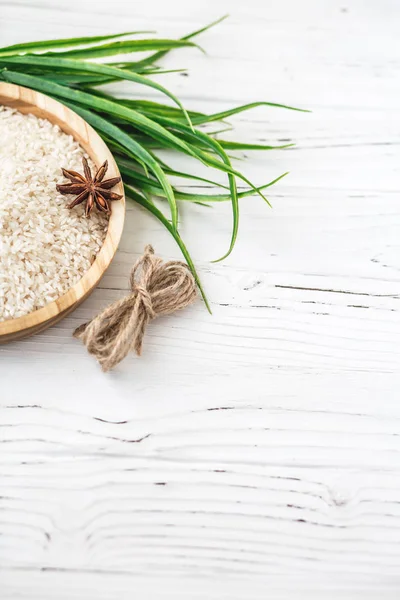 Arroz en plato de madera y anís sobre fondo de madera blanca. Arroz y especias en contenedor ecológico. Listos para cocinar. Set para spa . — Foto de Stock