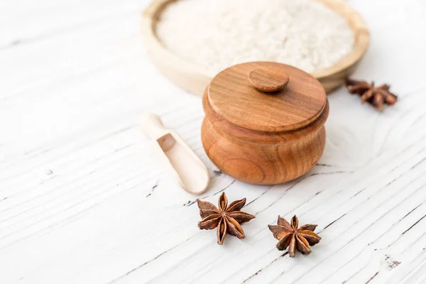 Arroz en plato de madera y anís sobre fondo de madera blanca. Arroz y especias en contenedor ecológico. Listos para cocinar. Set para spa . — Foto de Stock