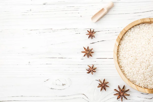 Arroz en plato de madera y anís sobre fondo de madera blanca. Arroz y especias en contenedor ecológico. Listos para cocinar. Set para spa . — Foto de Stock